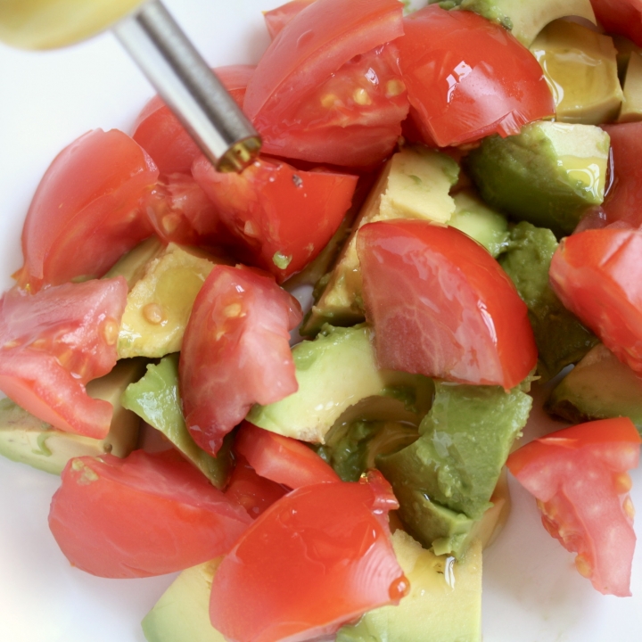 adding olive oil to avocado and tomato salad