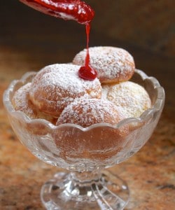 pouring raspberry sauce on pile of Aebleskivers in a crystal bowl