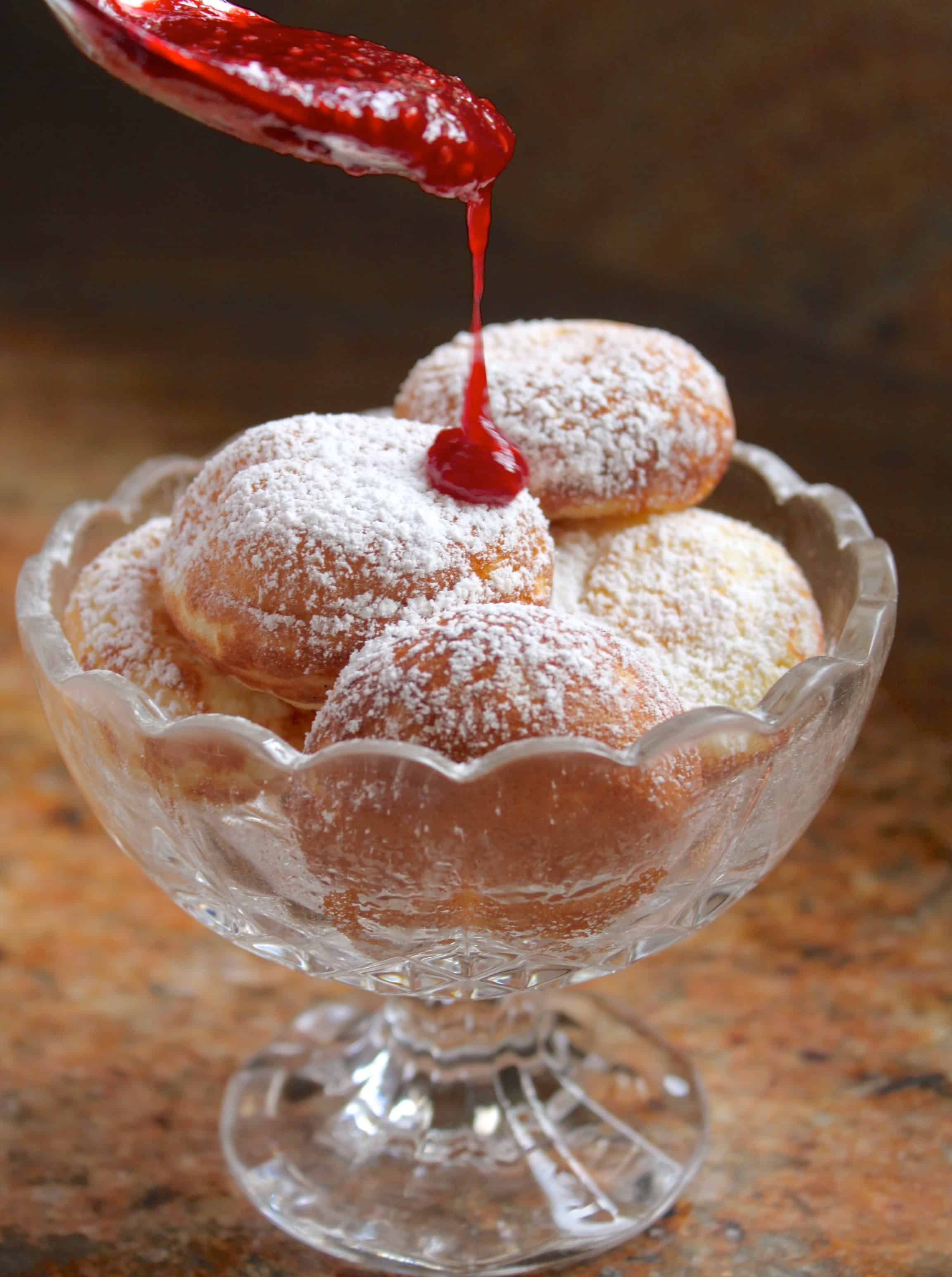 pouring raspberry sauce on pile of Aebleskivers in a crystal bowl 