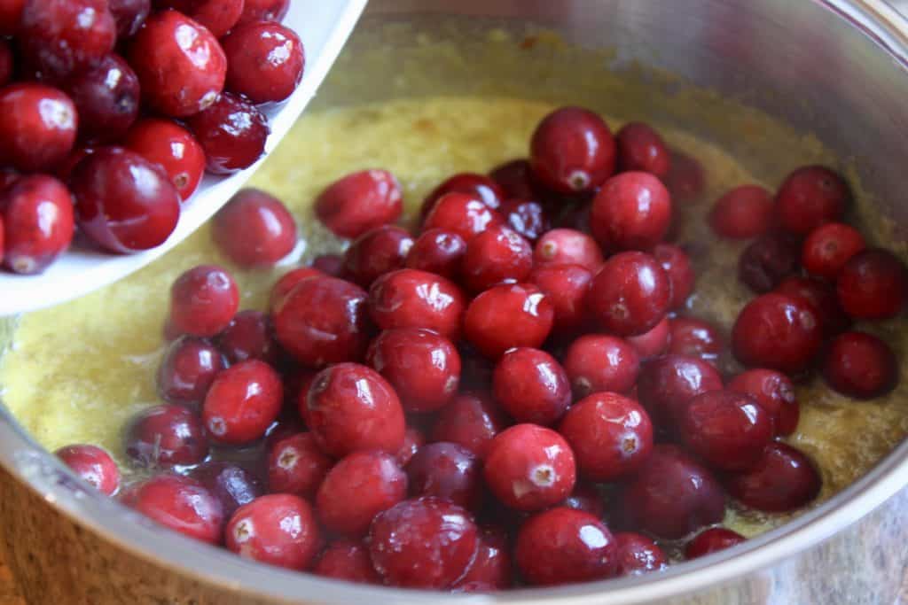 pouring cranberries into the mixture in the pot