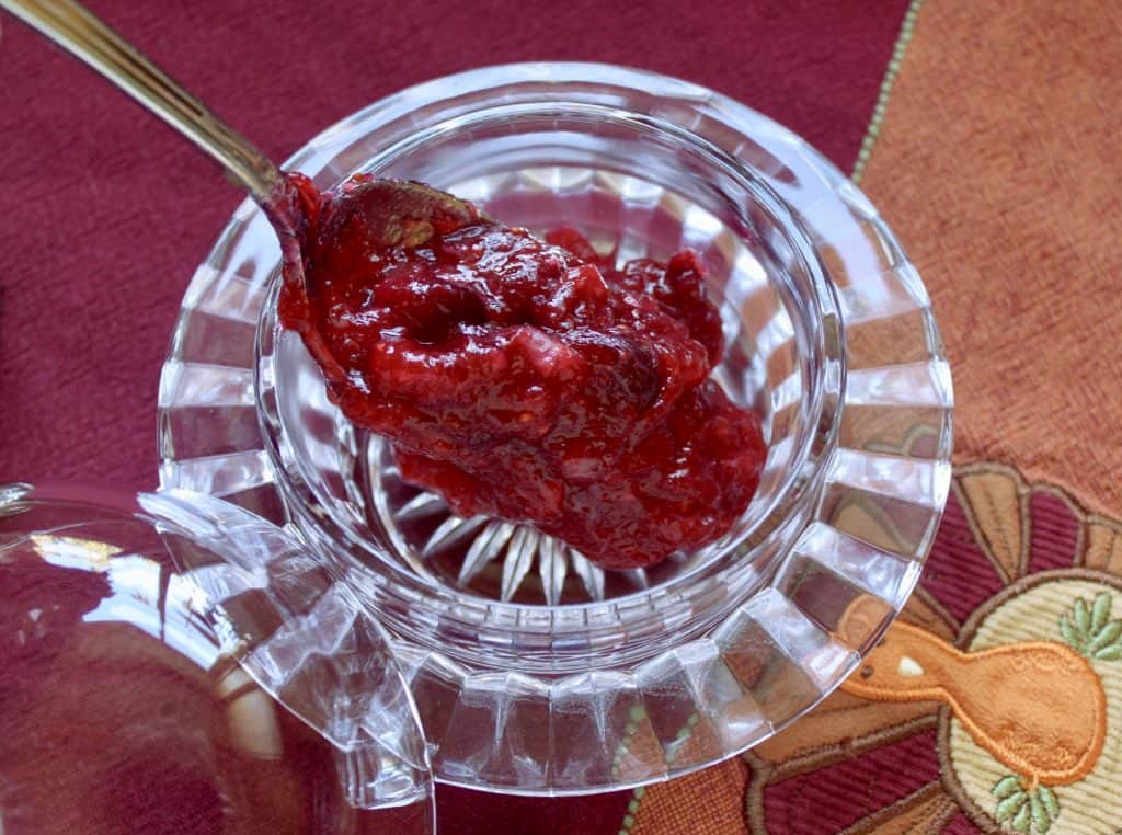 spooning orange Cranberry Sauce into a pretty glass bowl