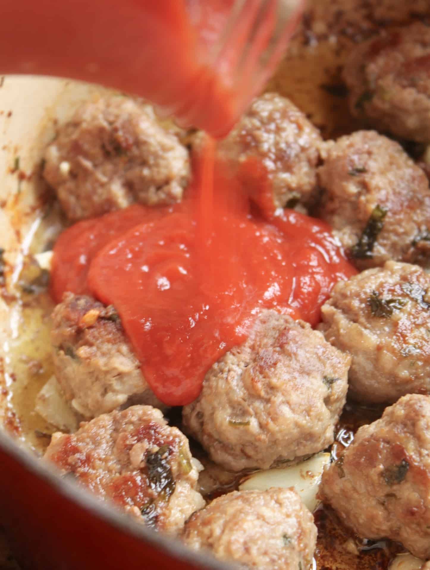 adding sauce to meatballs