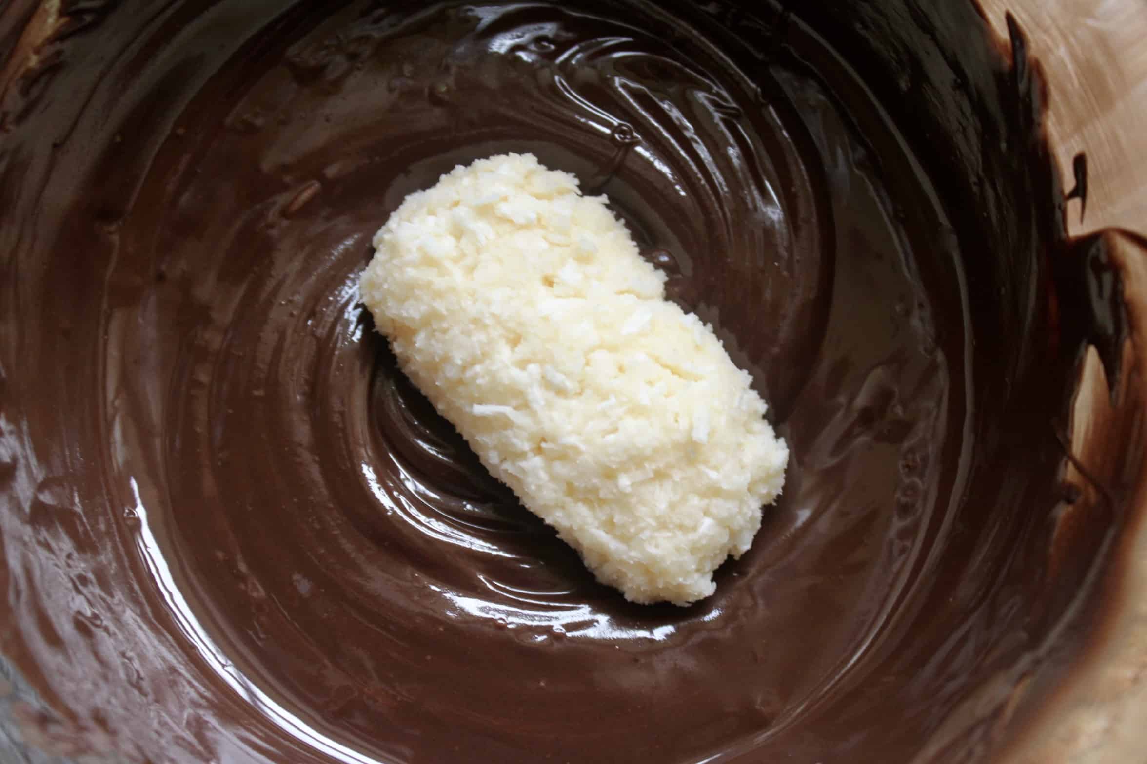 homemade coconut candy in a bowl of melted chocolate
