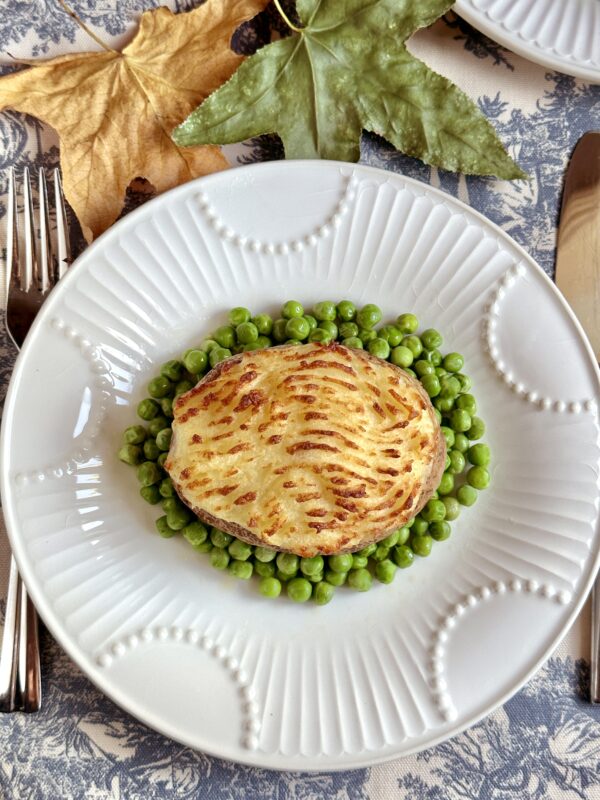 shepherd's pie baked potato on plate surrounded by peas