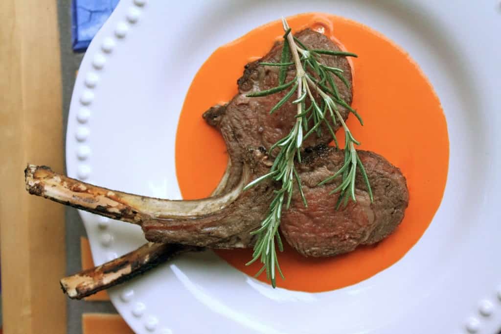 lamb chops on a plate with red pepper sauce and rosemary