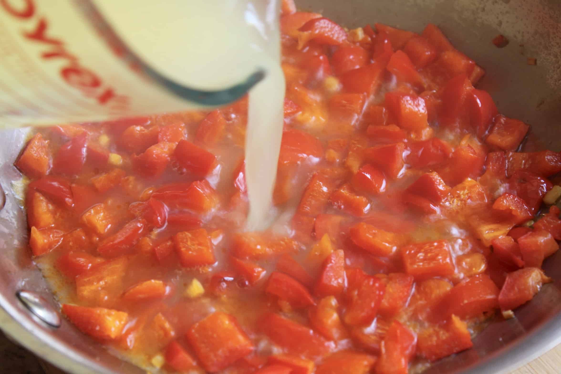 adding stock to peppers in pan