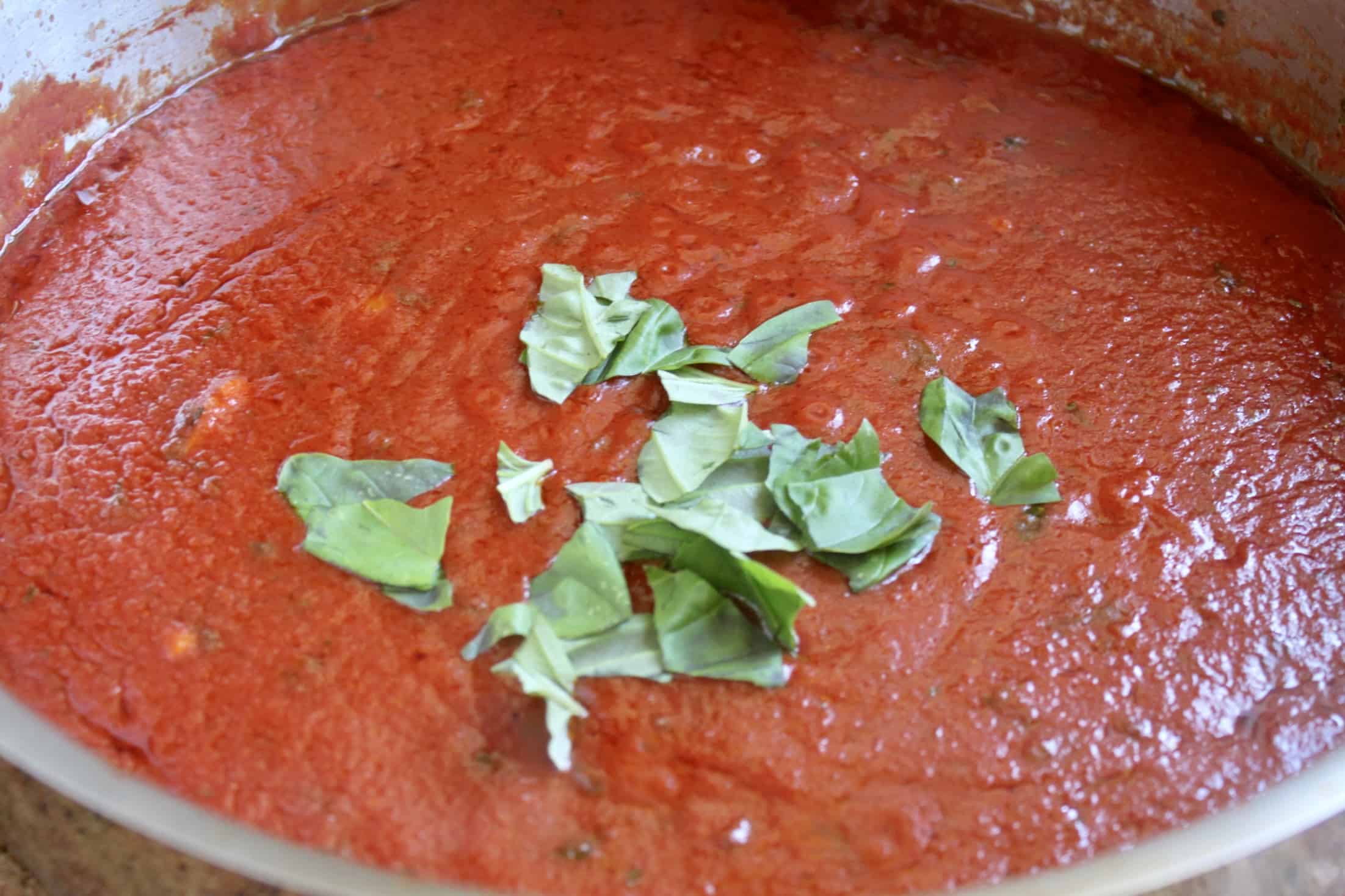 torn basil in a pan of Italian tomato sauce