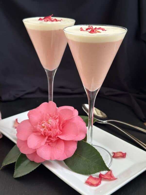 rhubarb fool topped with cream in two tall glasses with a pink camellia on the plate
