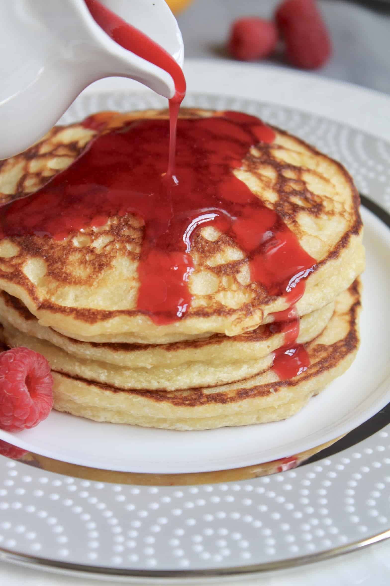 pouring rasberry syrup on lemon ricotta pancakes