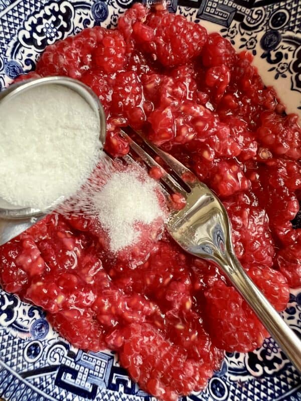 adding sugar to crushed raspberries