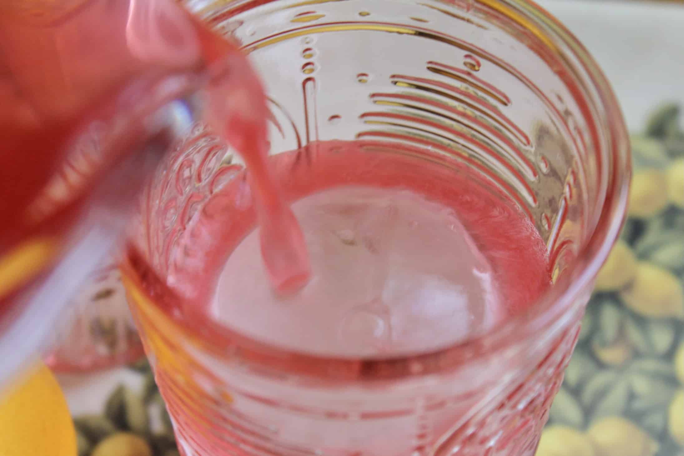 pouring cranberry lemonade over a large ice ball