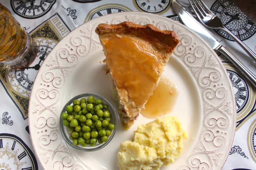 Chicken and leek pie on a plate with mashed potatoes and peas