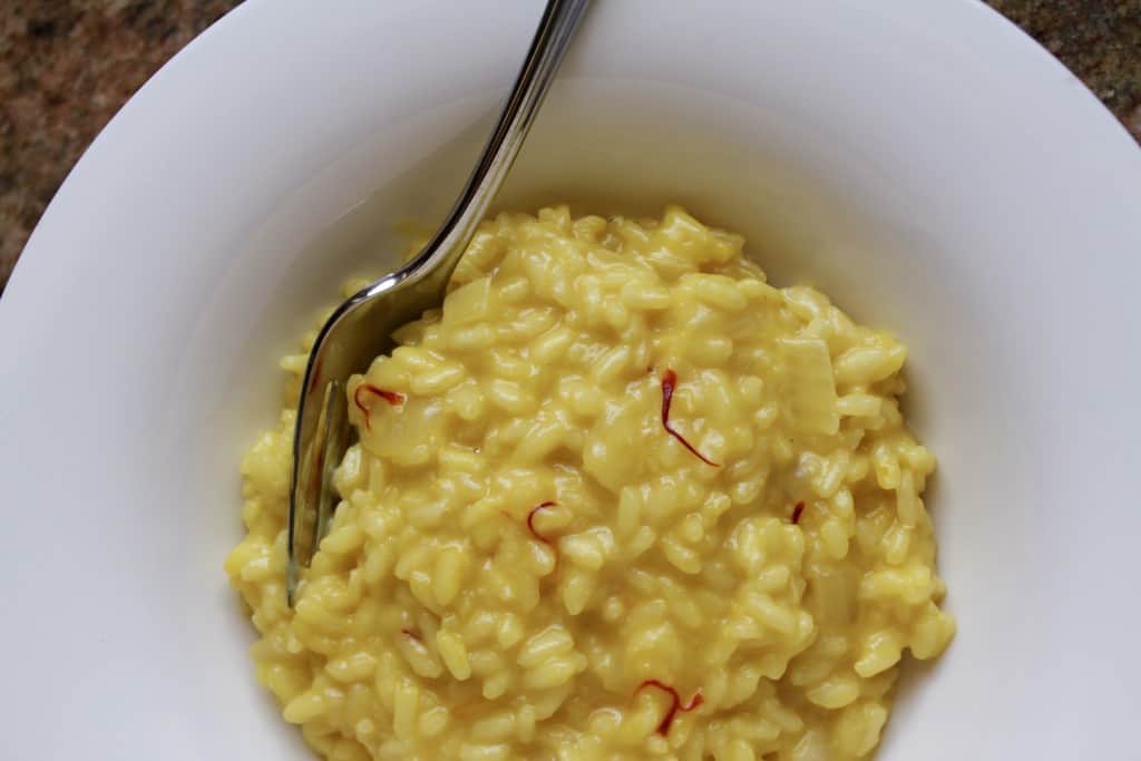 risotto alla milanese in a white bowl with a fork