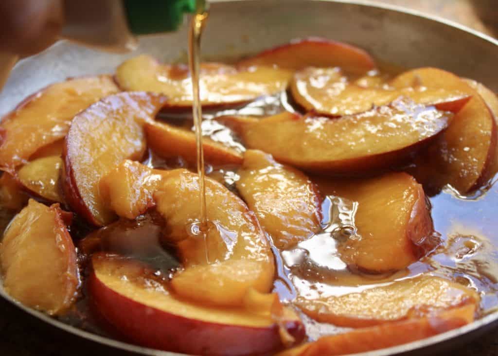 pouring maple syrup onto peaches in pan
