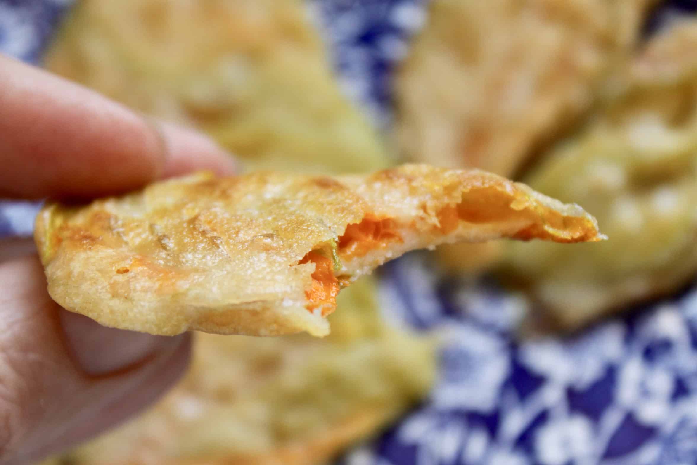 handheld fried zucchini flower with a bite taken