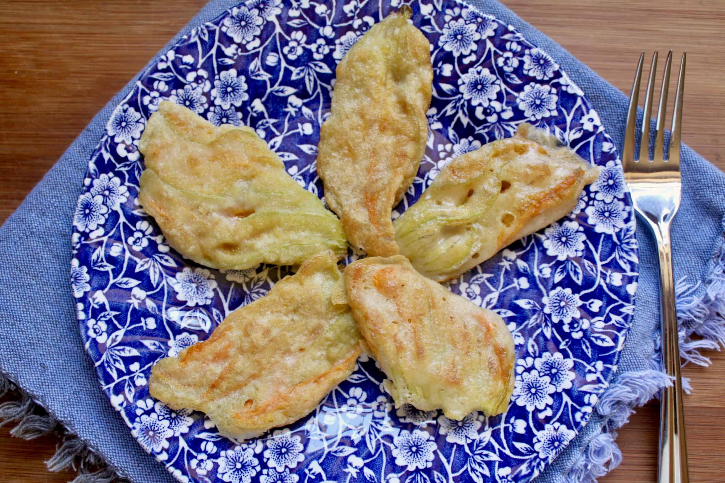 5 fried Italian zucchini blossoms on a floral plate