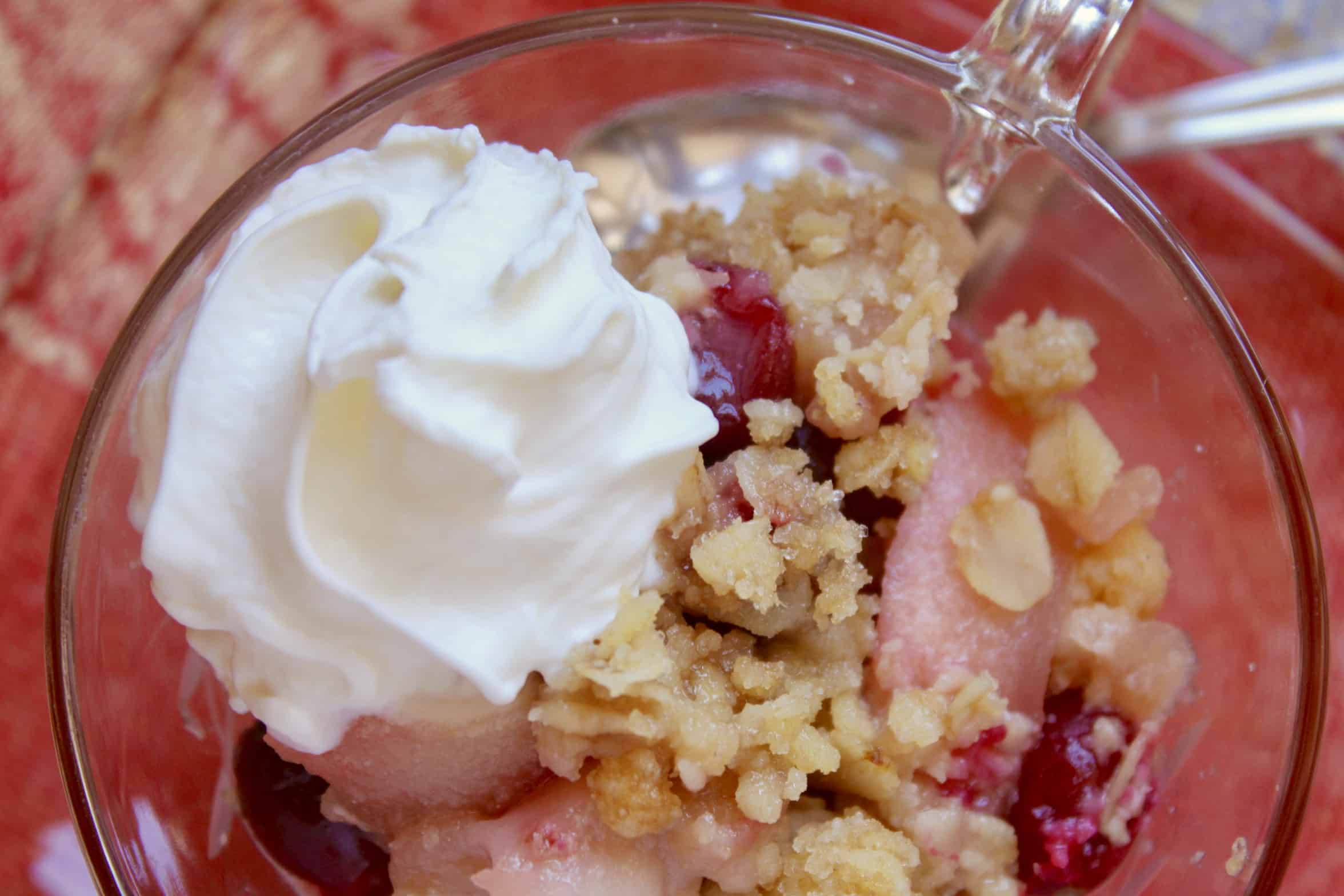 apple cranberry crisp in glass cup and saucer with cream