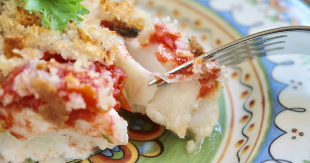 Oven baked fish on a plate with a fork pulling the flakes