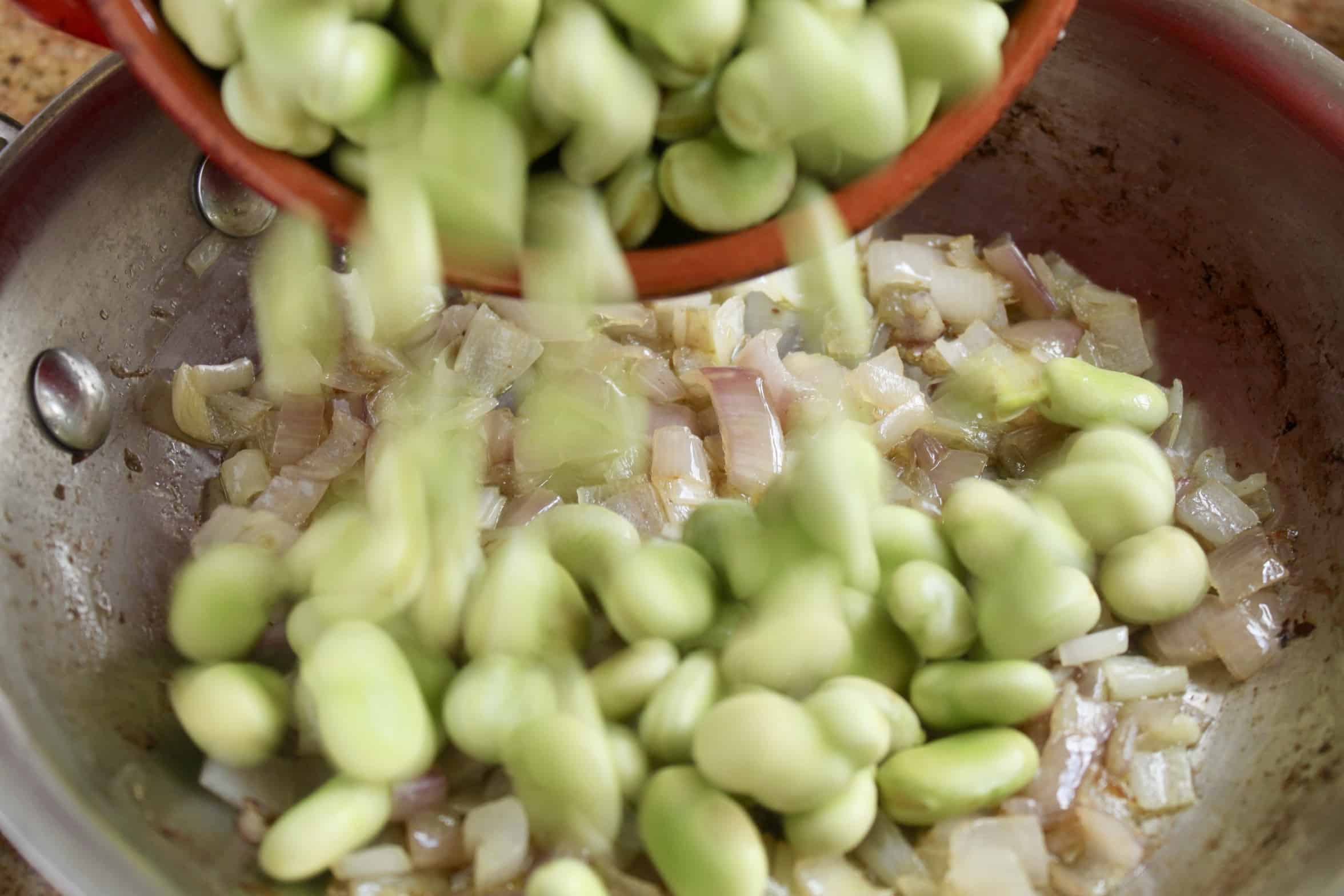 fava beans being added to pan