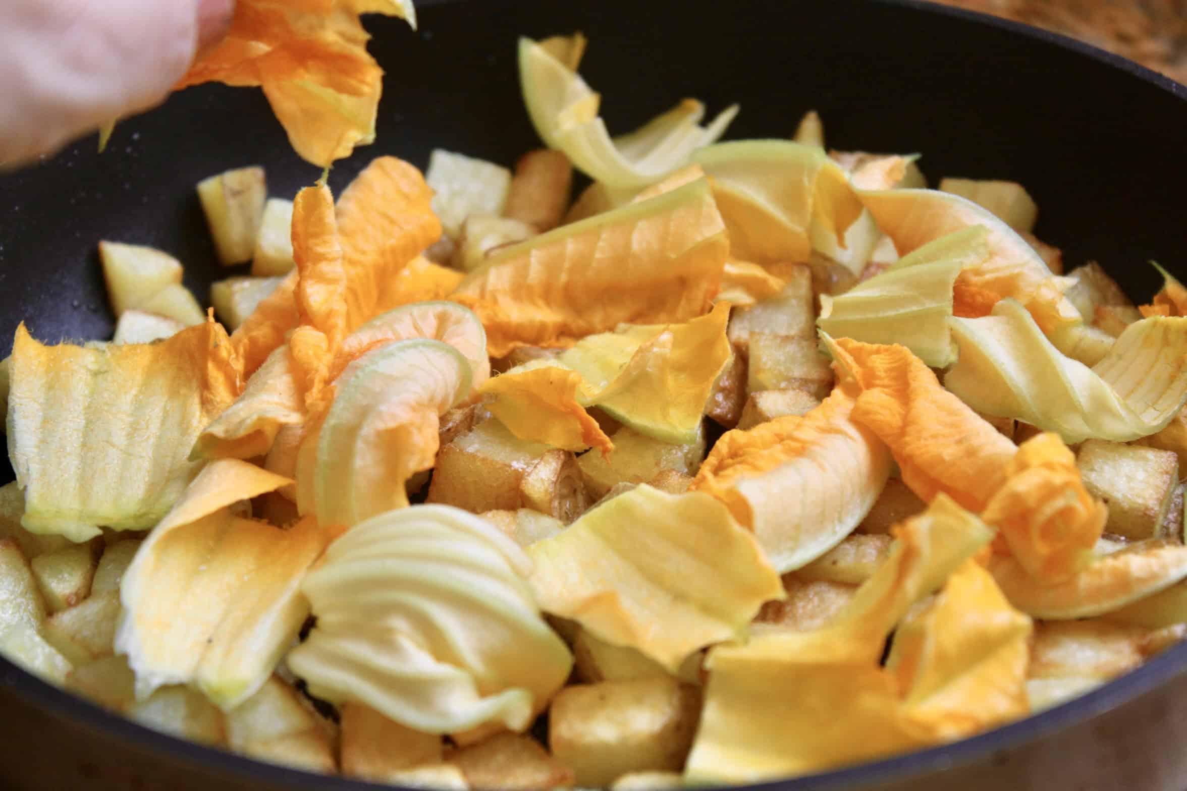 adding zucchini blossoms to potatoes in pan