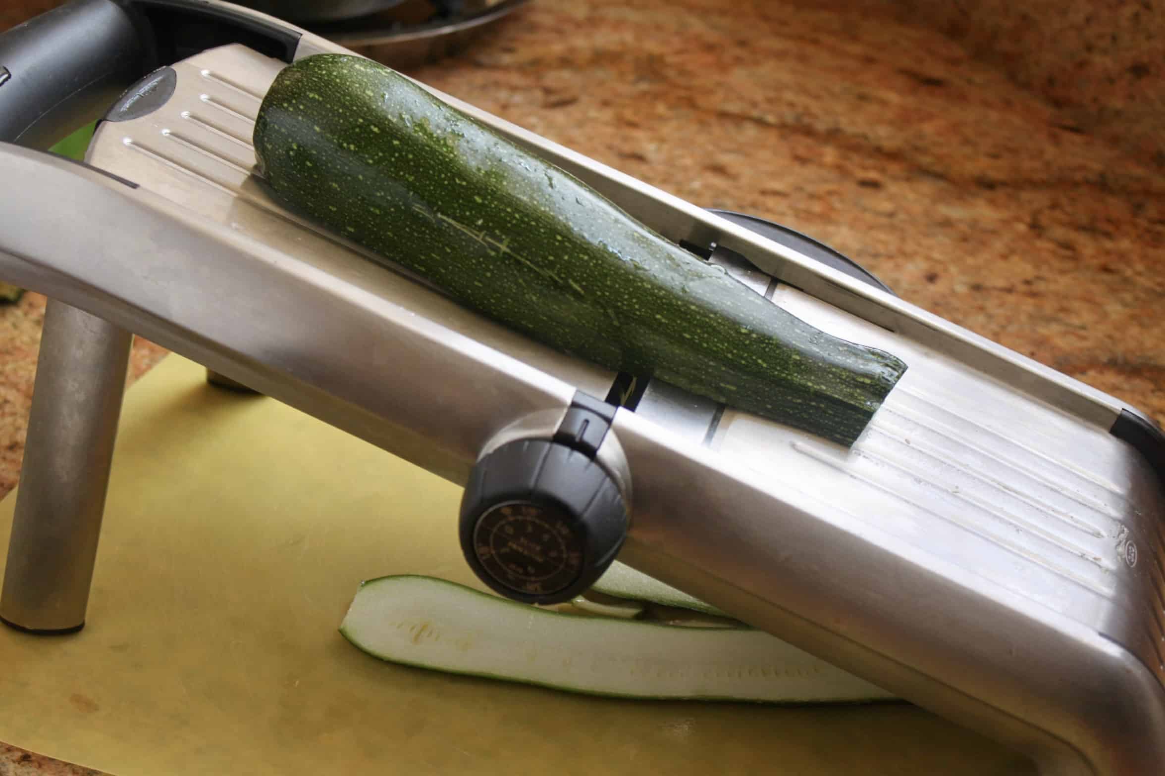 slicing zucchini on a mandoline slicer