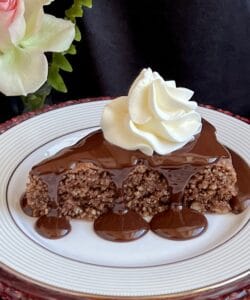 chocolate sauce poured over a slice of hazelnut cake with whipped cream.