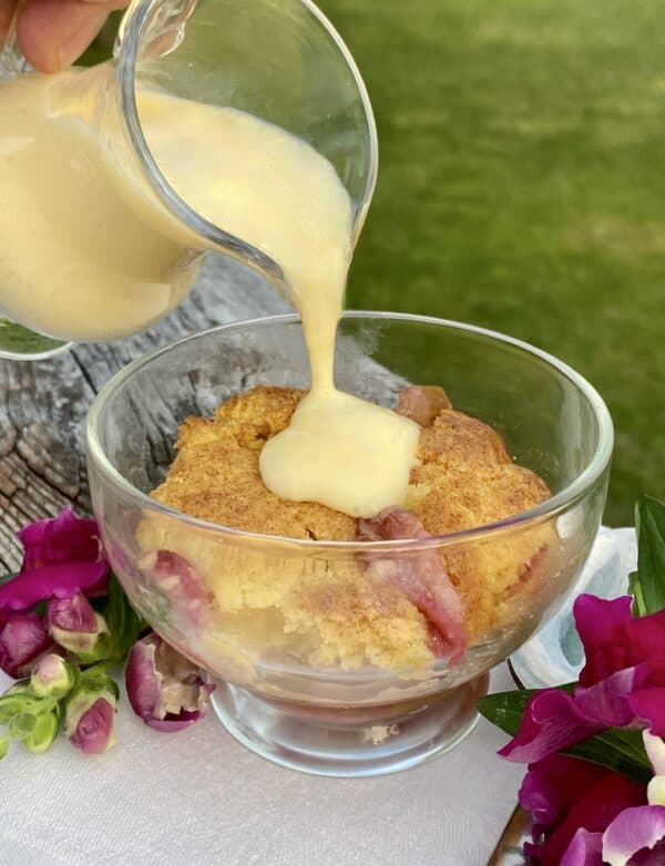 pouring custard over rhubarb cobbler