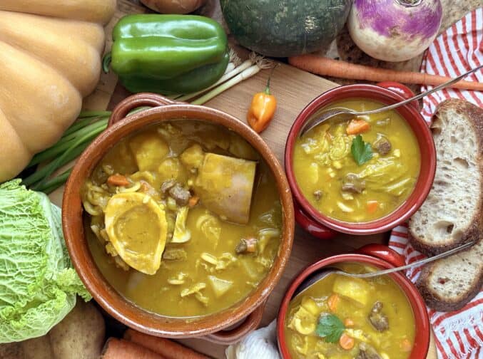 soup joumou in pot and bowls with vegetables