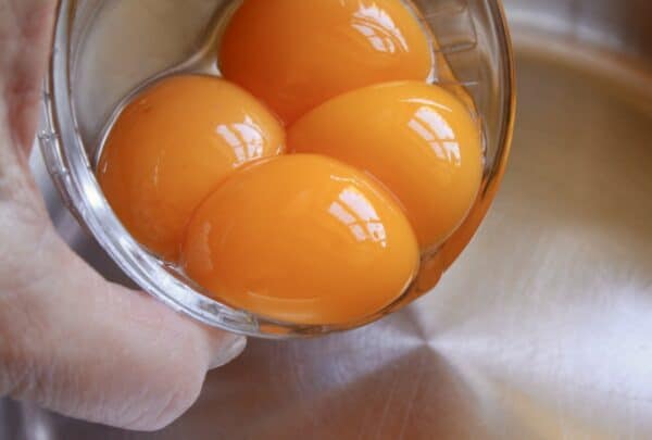 4 egg yolks being placed in a pot