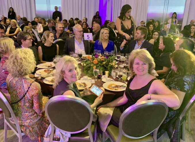 Cynthia Woodman and Christina Conte seated at a James Beard dinner in Los Angeles with Curtis Stone