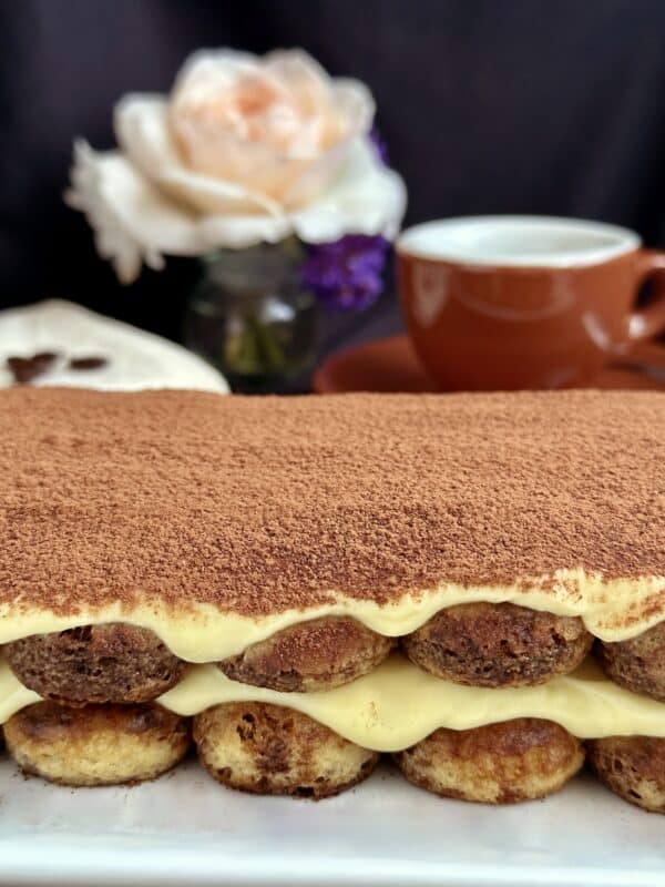 original tiramisu on a plate with a rose and espresso cup