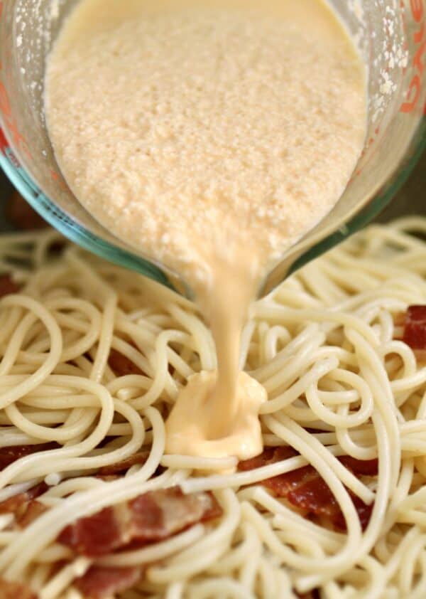 pouring cream mixture into pasta with egg and bacon