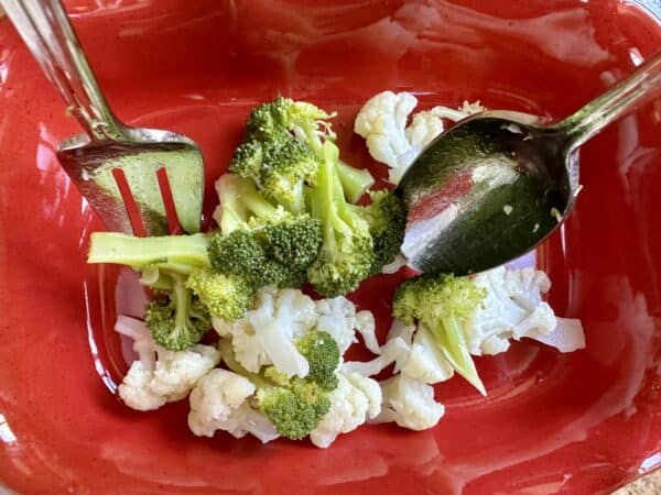 adding the broccoli and cauliflower salad to a red dish