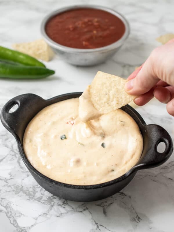Queso blanco with a hand dipping a chip into the bowl