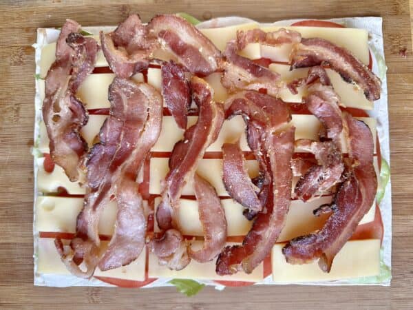 adding bacon onto pinwheel sandwiches