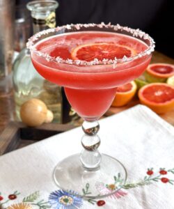blood orange margarita on embroidered tea towel with tequila nearby