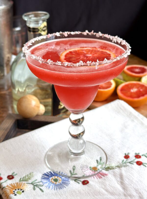 blood orange margarita on embroidered tea towel with tequila nearby
