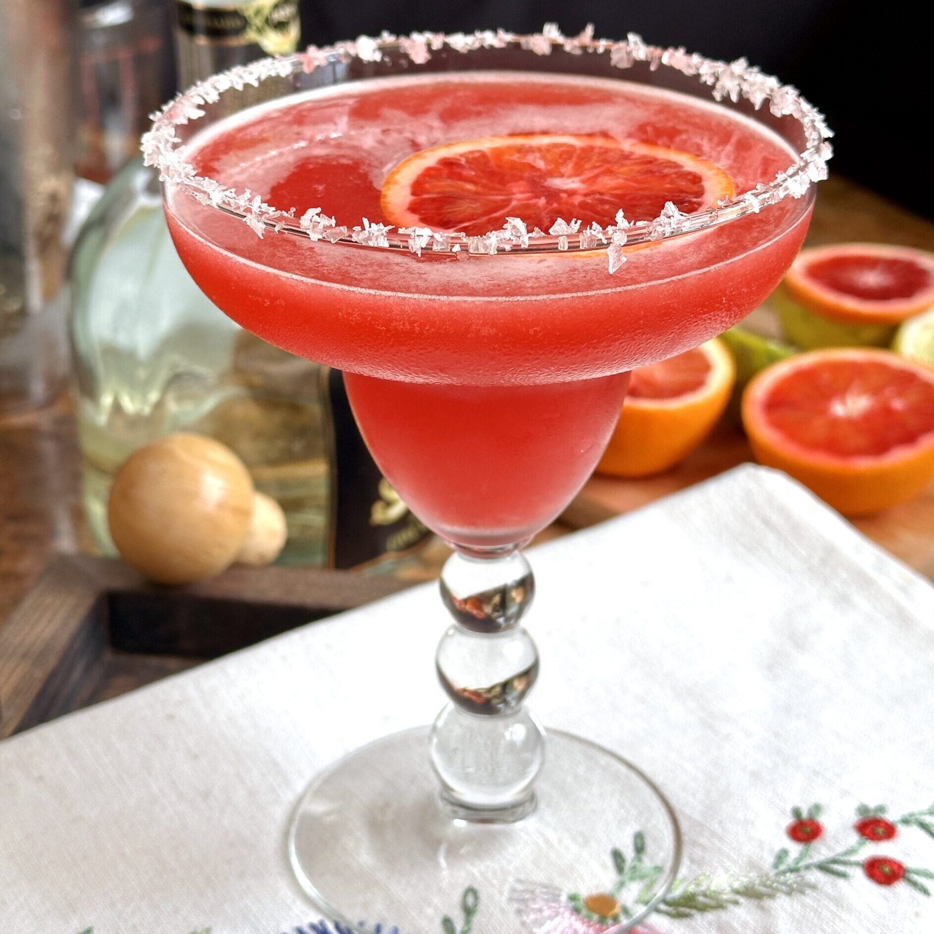 blood orange margarita on embroidered tea towel with tequila nearby