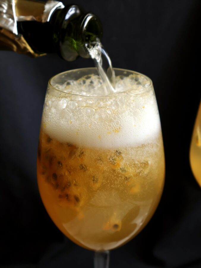 pouring Prosecco into passion fruit cocktail