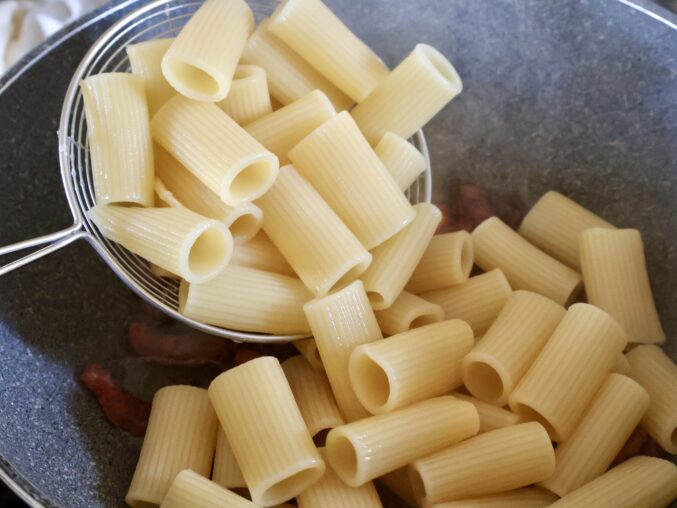 adding rigatoni to guancial in pan
