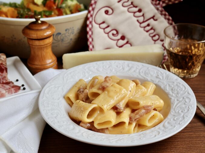 rigatoni alla carbonara in a bowl with pepper grinder and cheese