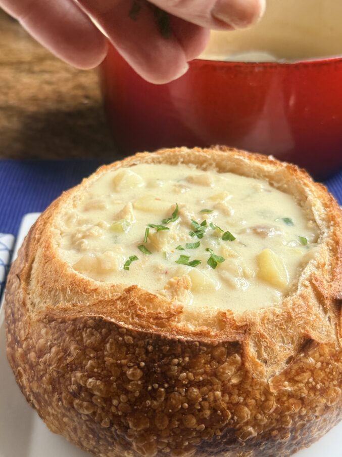 sprinkling parsley on San Francisco clam chowder in sourdough boule