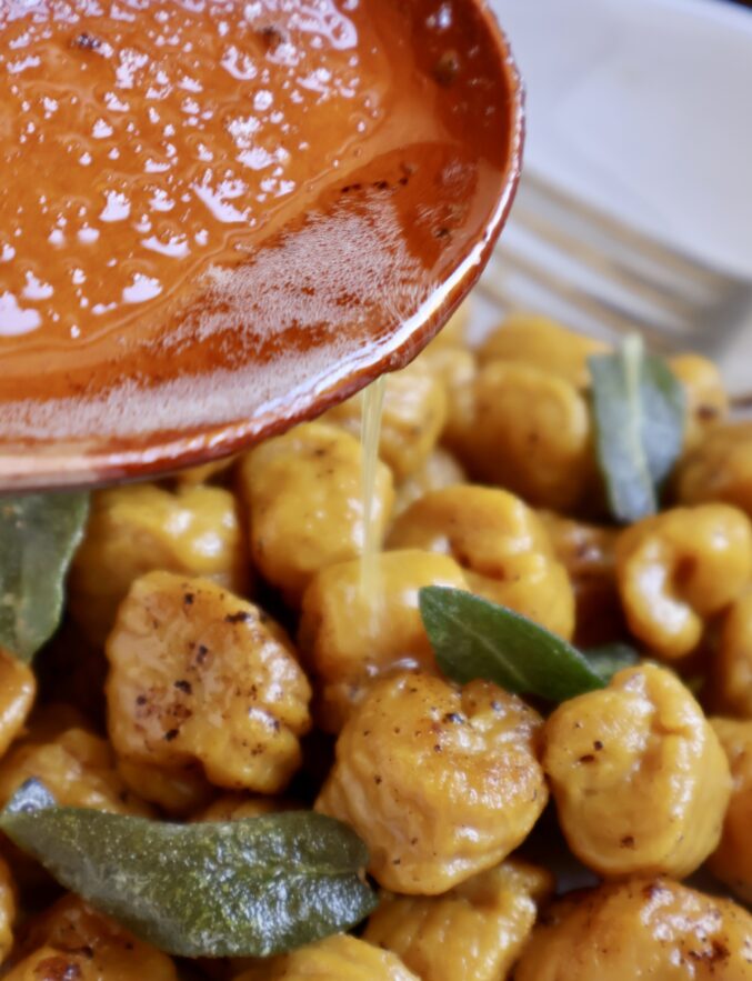 pouring brown butter sauce over pumpkin gnocchi